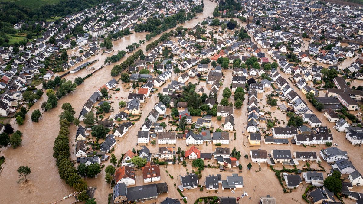 Aerial view of muddy-looking floodwaters from a meandering river flooding houses and buildings throughout a town spread on either side of the river