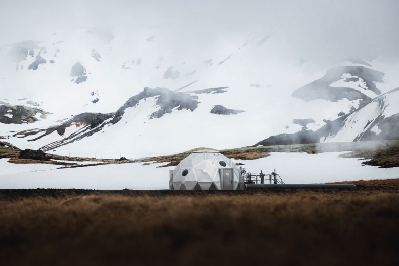 Ground-level view of a metal dome-shaped structure with snow-covered mountains in the background.