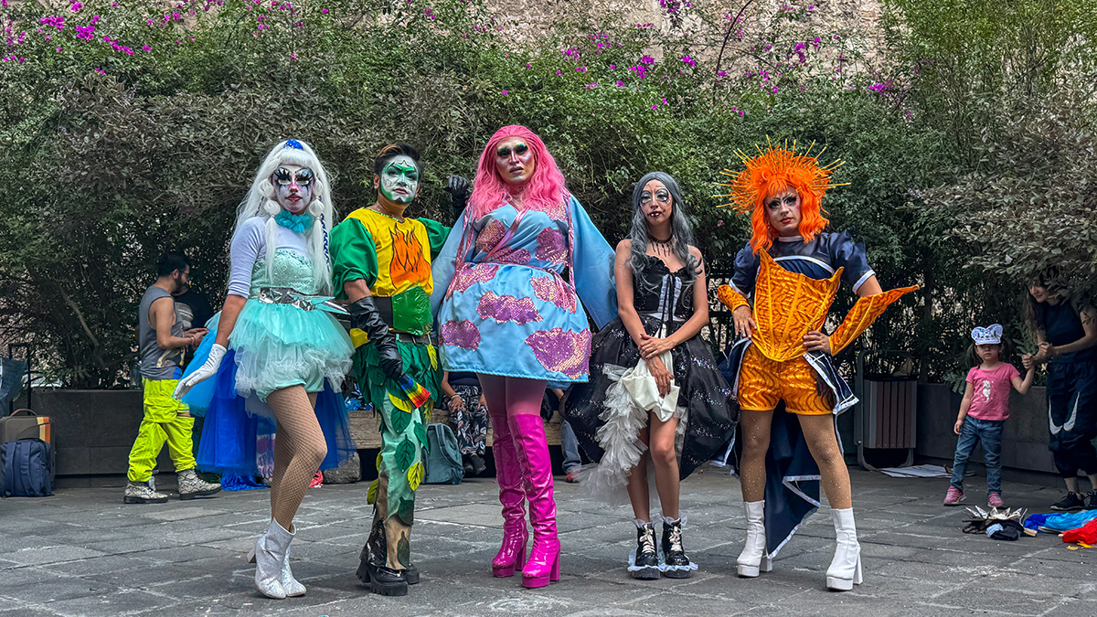 Cinco personas posan para la cámara con mucho maquillaje y vestuarios coloridos.