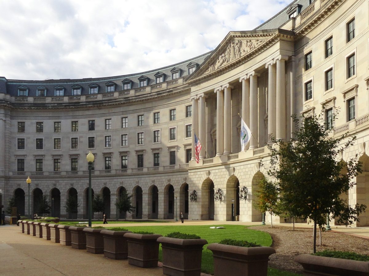 A curved building with classic pillars is seen from the sidewalk.