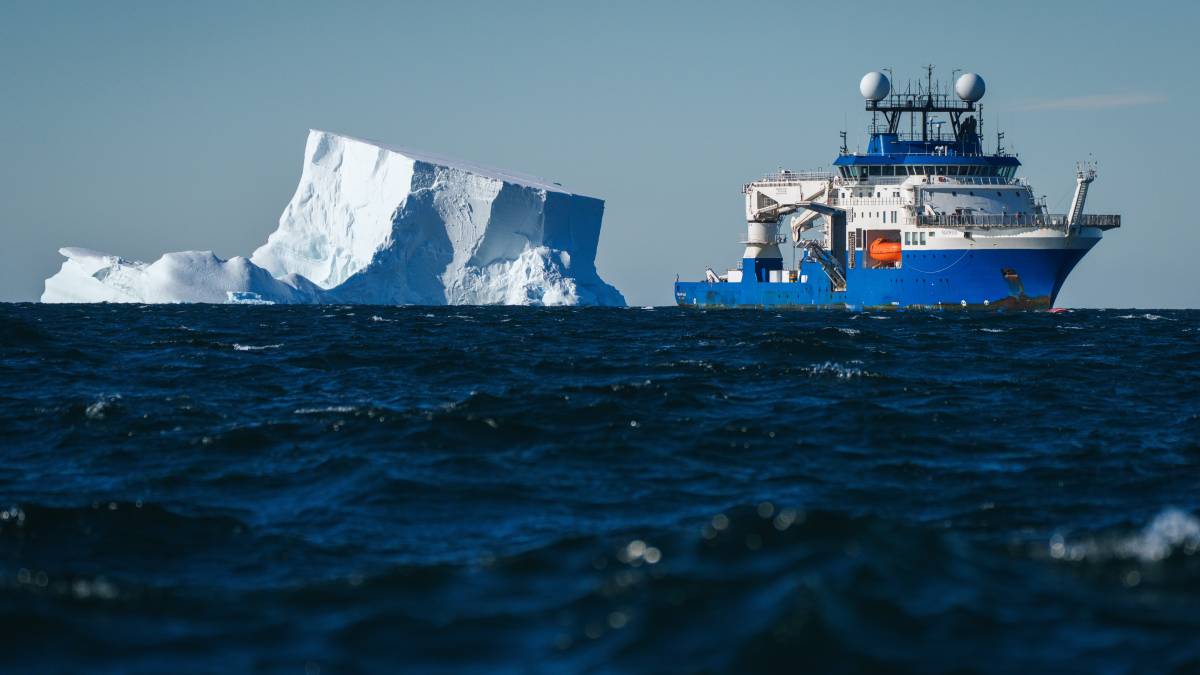 View from afar of a blue and white research vessel next to an iceberg.