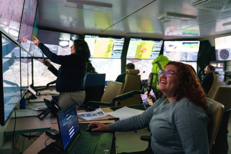 People surrounded by computer monitors in a darkened room