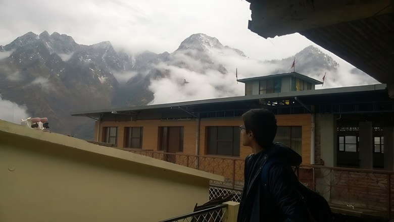 A person looks over the roofs of buildings toward mountains shrouded in clouds.