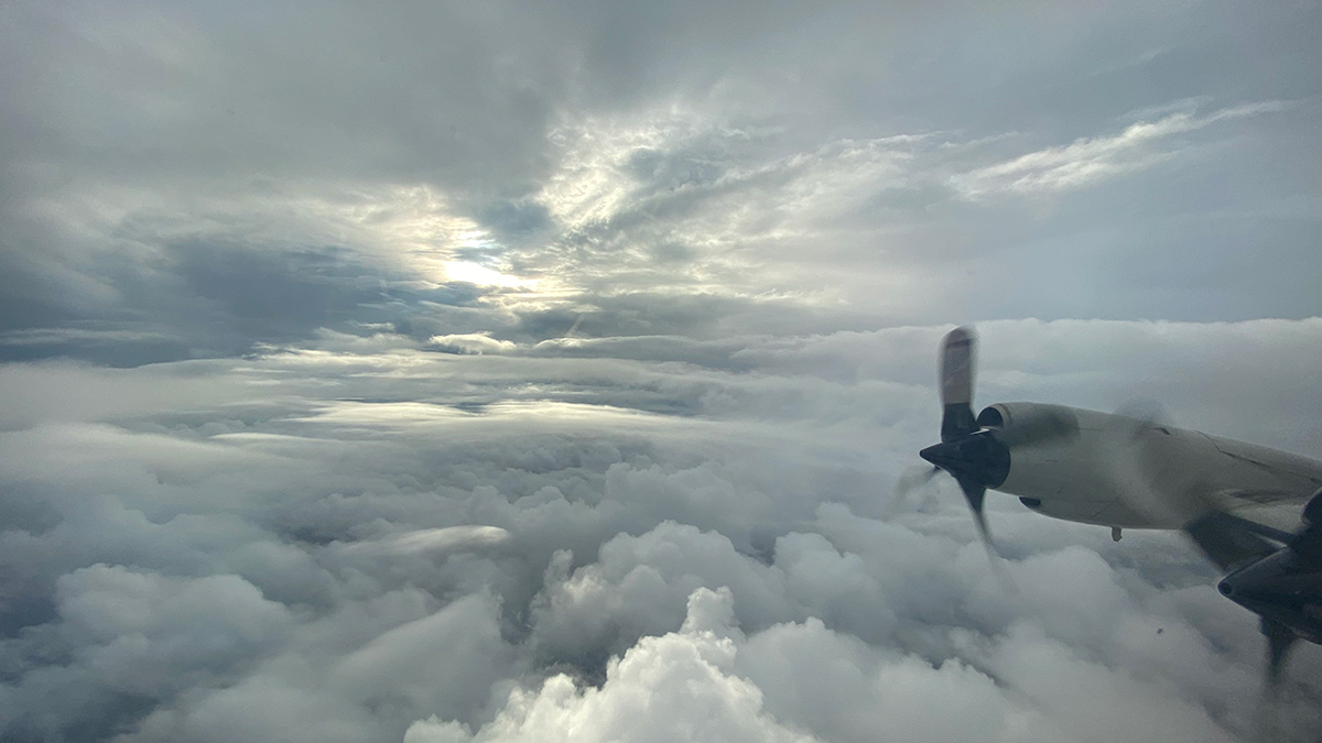 The wing of an airplane and a propeller are visible against a cloud-filled sky.