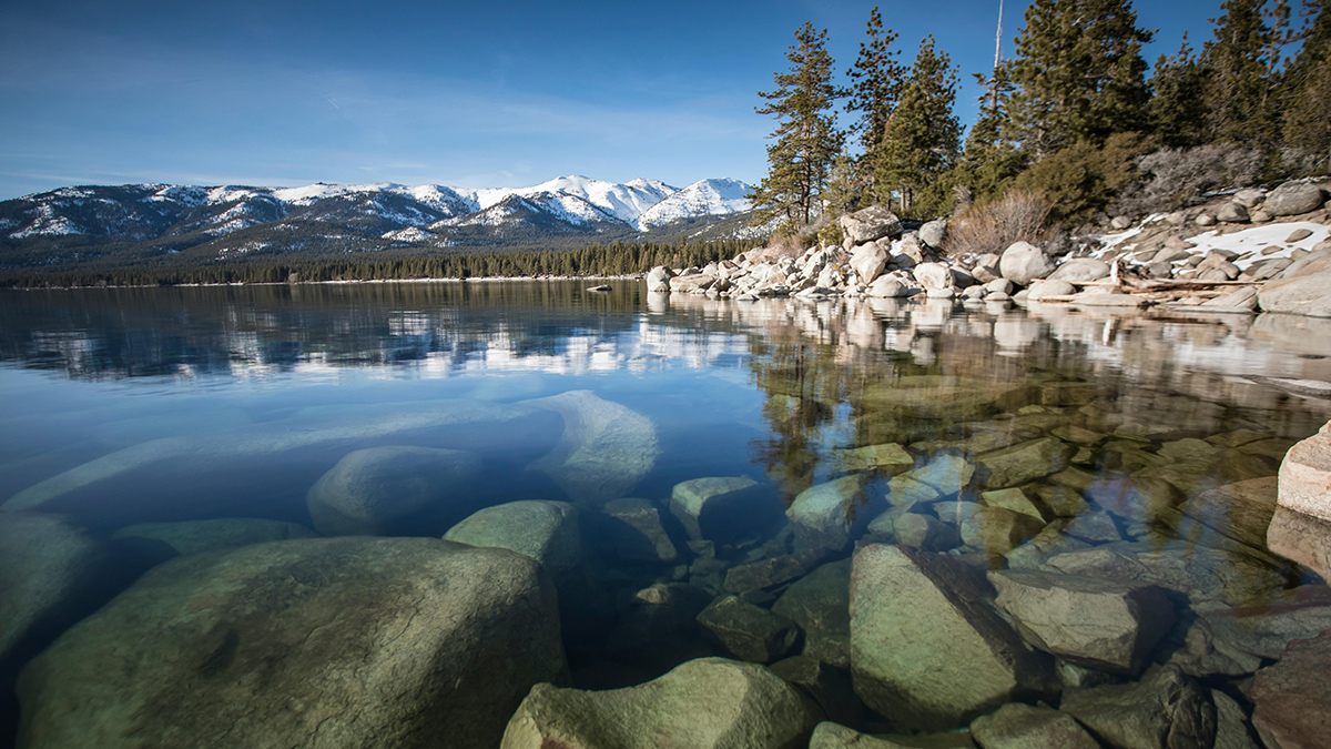Clear water in Lake Tahoe with granite boulders and Sierra Nevada mountains in the background