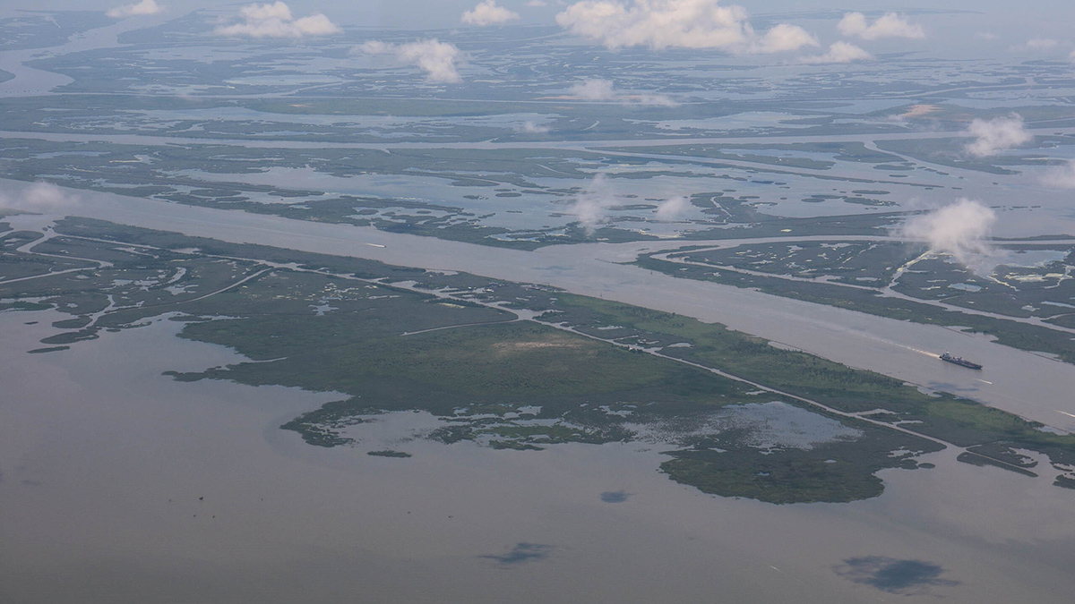A bird’s-eye view of the Mississippi River delta. The main river runs left to right across the photo and wispy clouds are visible in the foreground.