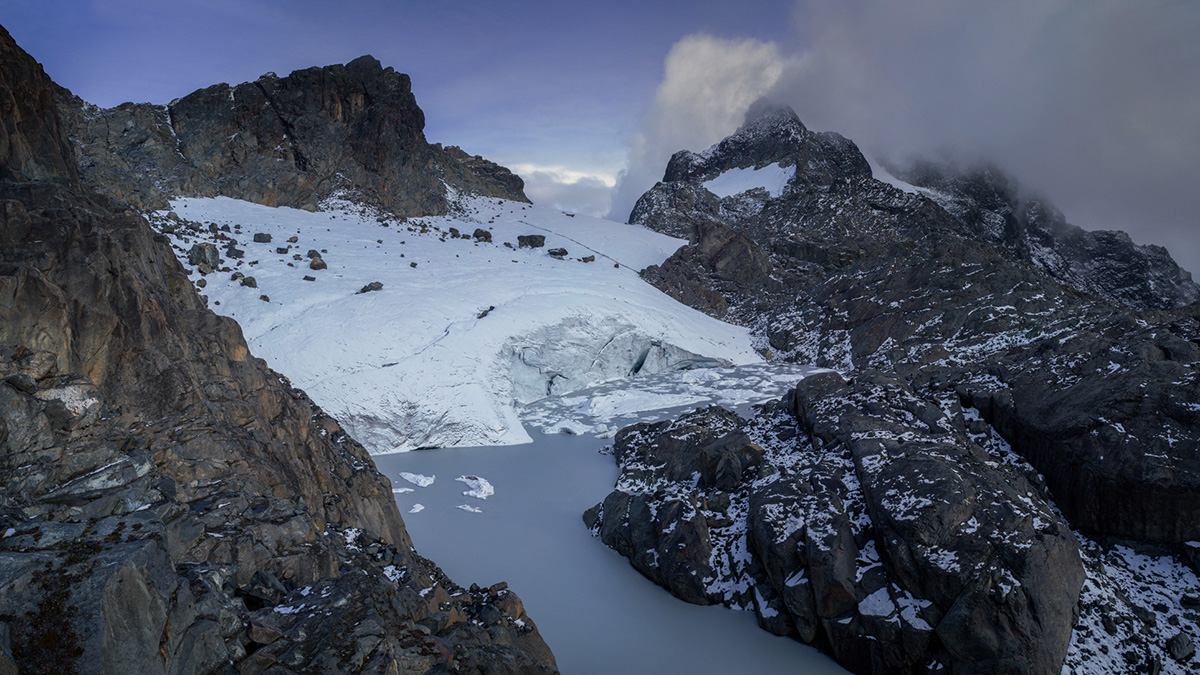 A glacier sits atop a jagged gray mountain.