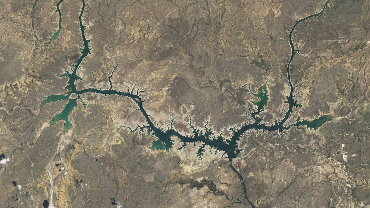 A satellite image of dry, brown land with a blue-green river winding horizontally through the center of the image.