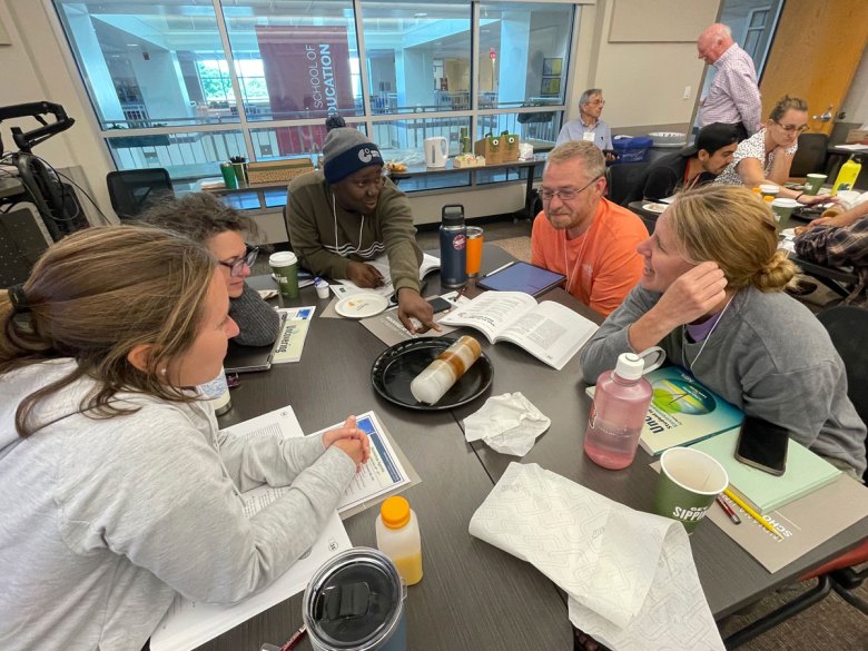 A group of five individuals sit around table discussing a model of an ice core sitting on a plate in the middle of the table.