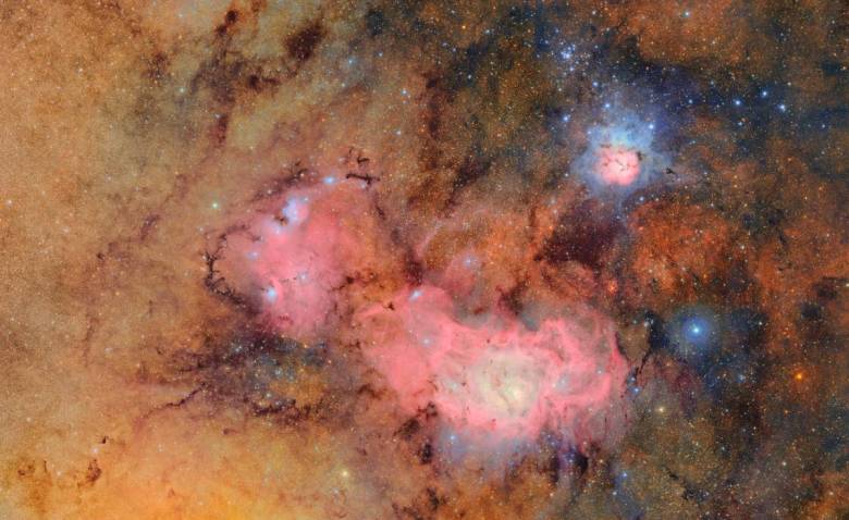 A cosmic tapestry of glowing tan and pink gas clouds with dark dust lanes.